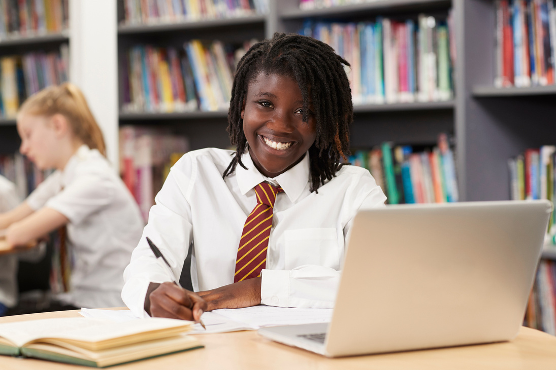 Portrait Of Female High School Student Wearing Uniform Working At Laptop In Library