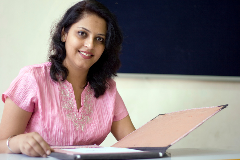 Young Attractive Indian Teacher sitting in a Classroom Blackboard File